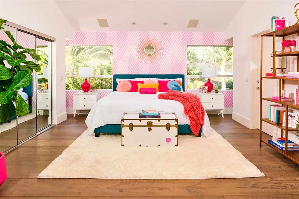 Modern bedroom featuring a white bed with pink and blue accents, surrounded by white furniture and a pink striped accent wall