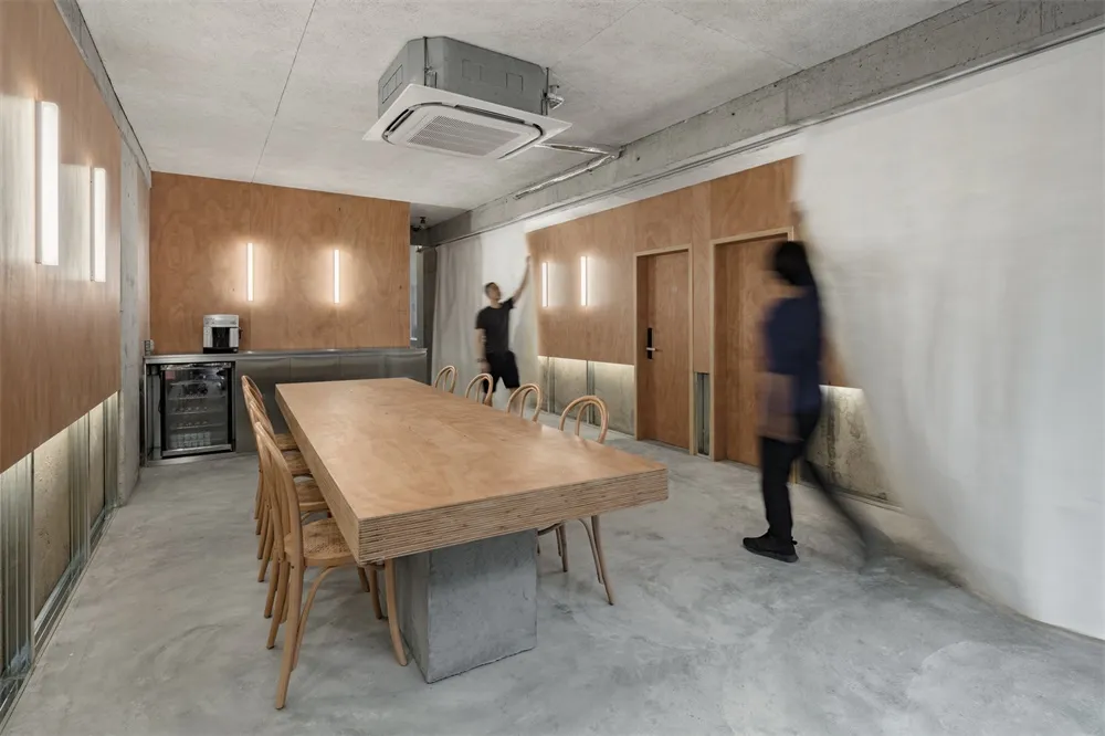 寬敞的工業風辦公室,混凝土地板、合板牆面與鋼製燈具,搭配大型木桌