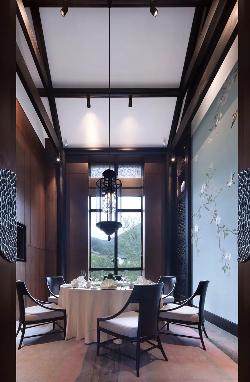 An elegant dining room featuring Asian-inspired decor with wooden furnishings, glass chandelier, and fabric seating.
