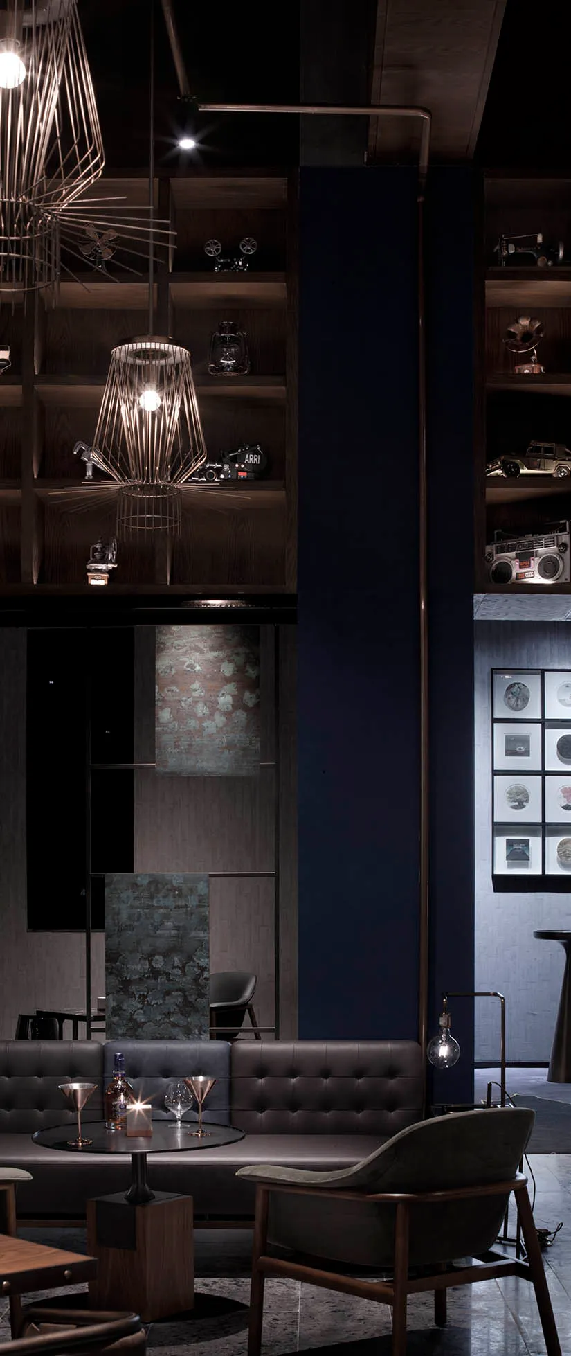 A modern restaurant bar setting with metal pendant lights, wooden shelves, and leather seating.