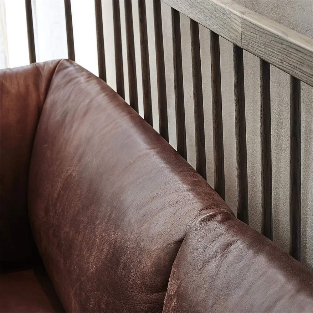 Brown leather sofa with dark wooden slats in an industrial setting.