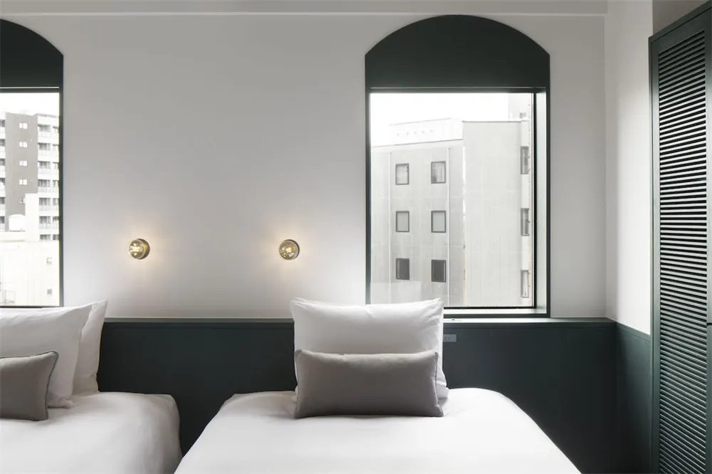 A minimalist hotel room with white walls and bedding.
