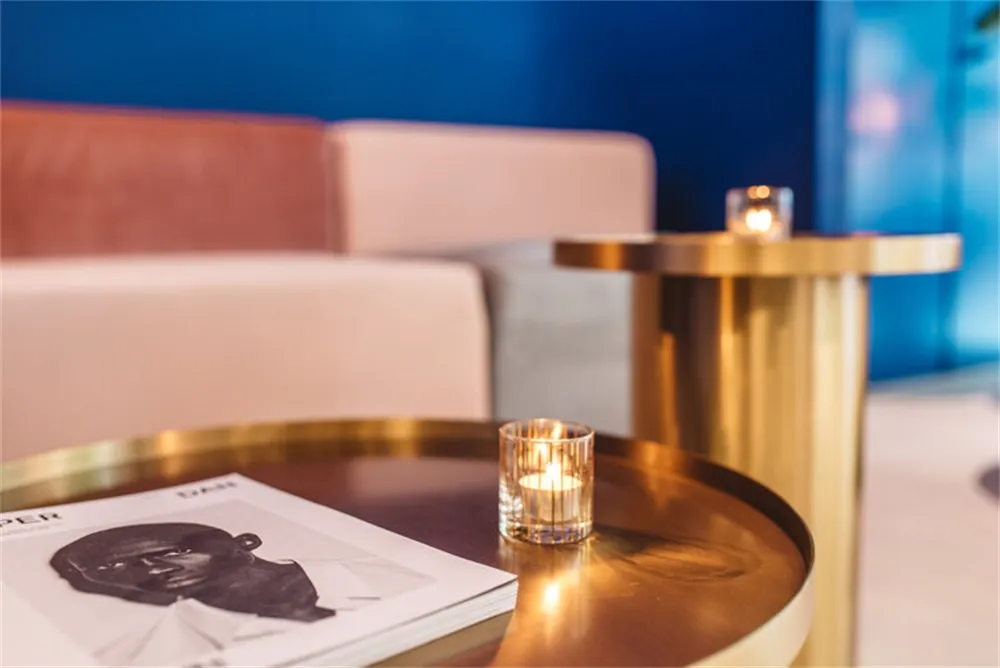 A modern coffee shop featuring metallic furniture with a lit candle and a magazine on a table.