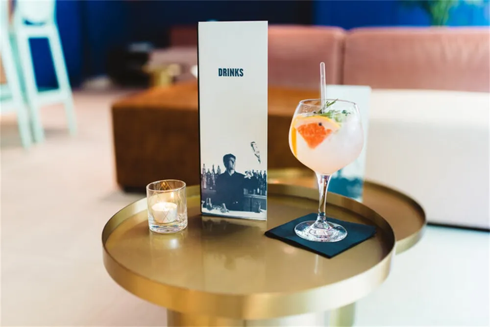 Modern, minimalist drink bar table featuring a glass drink, a metal tray, and a candle on a glass holder.