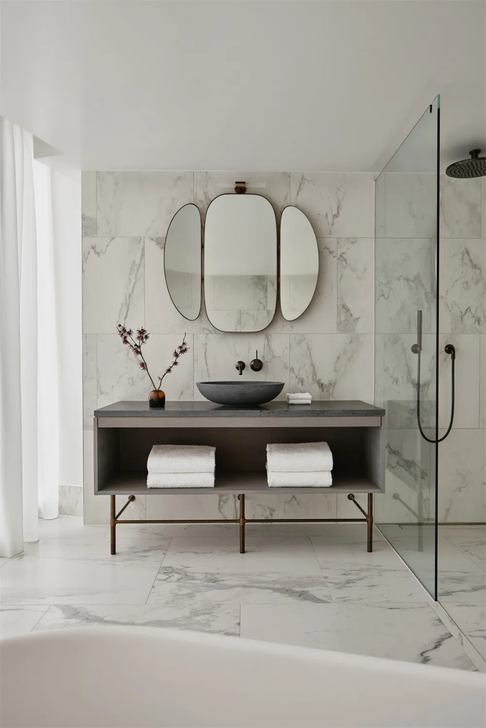 A modern bathroom with marble tile walls and floor, featuring a floating vanity, a black stone sink, and a walk-in shower wit