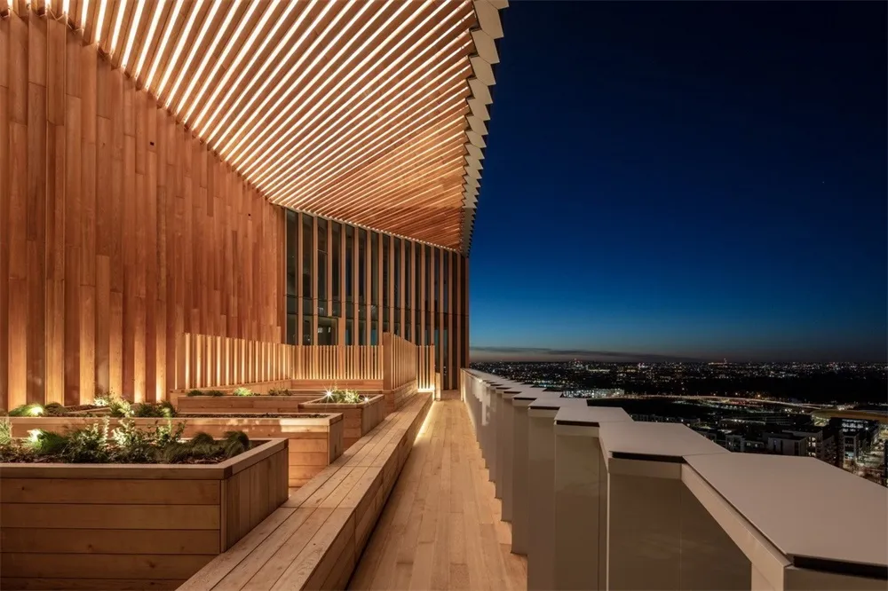 A wooden terrace with planters and a wooden structure at dusk overlooking a cityscape.