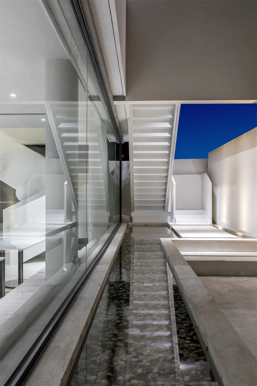 Modern minimalist interior space featuring a concrete pond and stairs, with a glass wall and a blue sky background.
