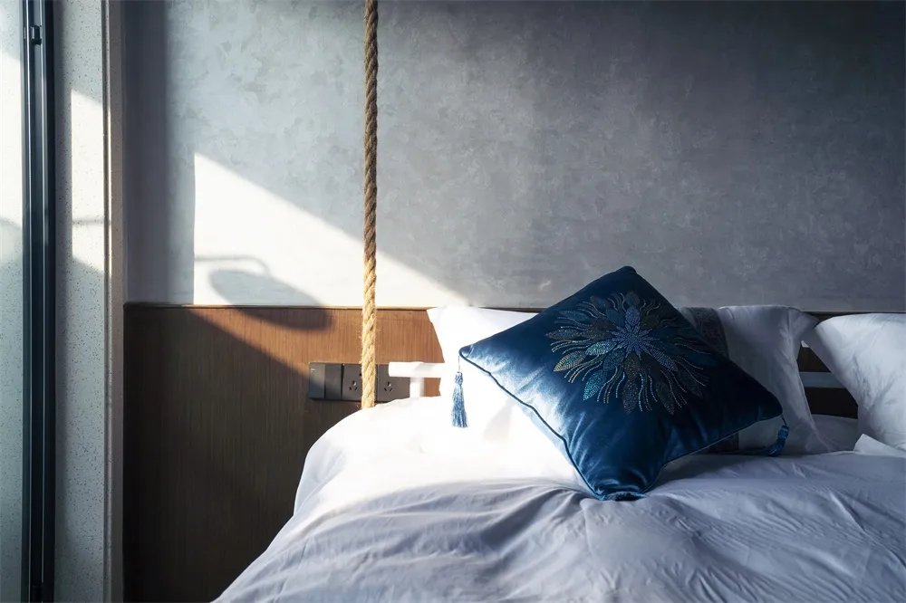 A modern bedroom with white cotton bedding, a blue decorative pillow, and a wooden headboard.