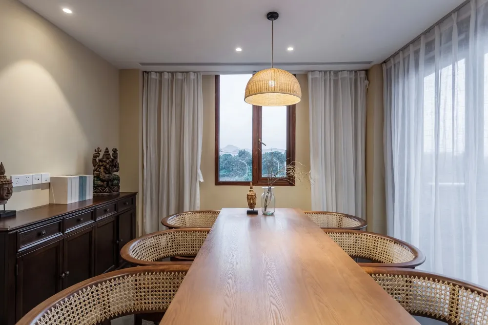Modern dining room featuring a large wooden table, wicker chairs, and a view through the window.