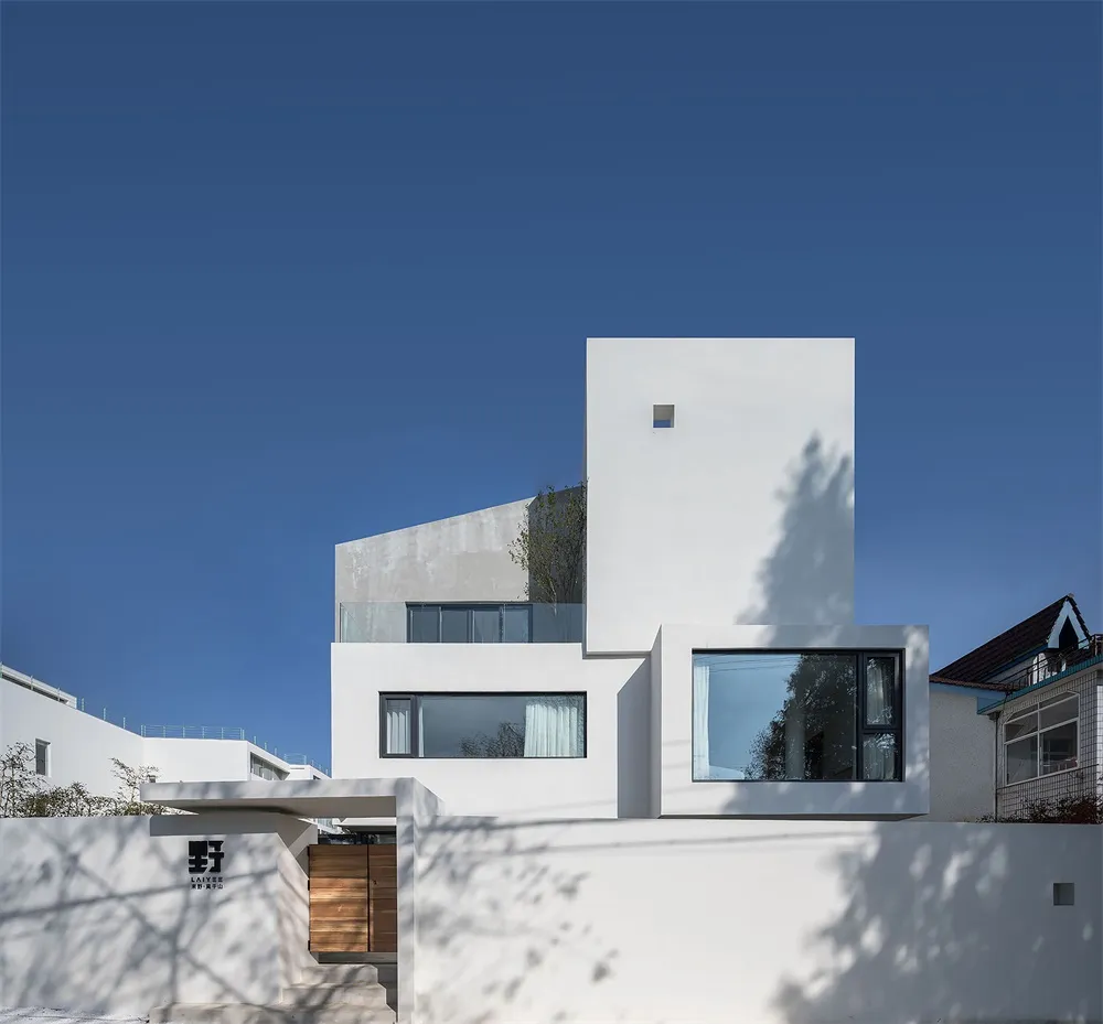 Modern residential exterior with white concrete walls and glass windows.