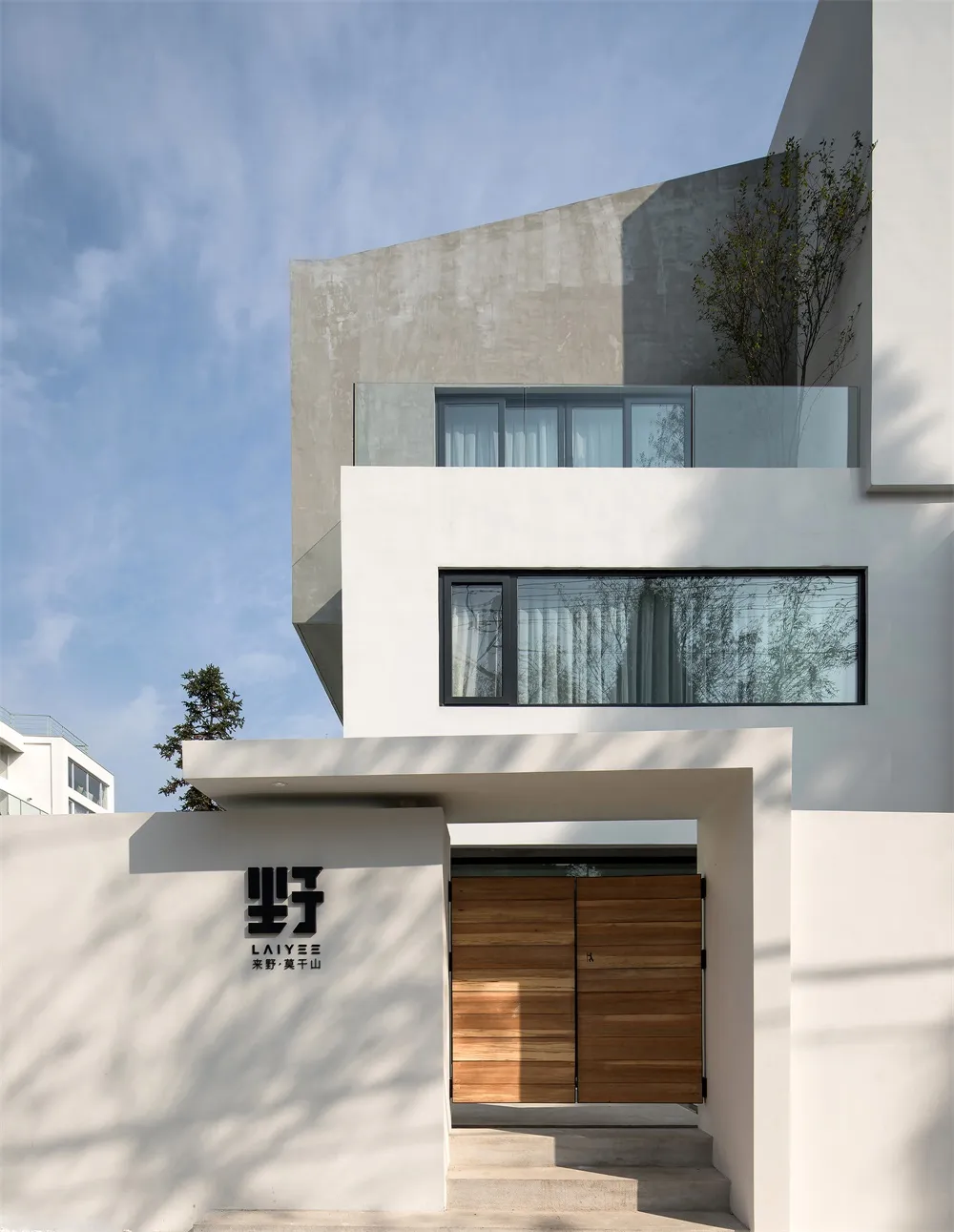 A modern minimalist house with a concrete exterior and glass balcony.