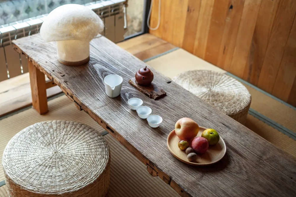 A serene tea ceremony room with wooden furniture, a teapot, and fresh fruits on a wooden table.