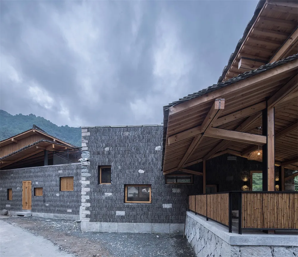 Contemporary residential home exterior featuring stone and wood materials, with a dramatic, cloudy sky in the background.