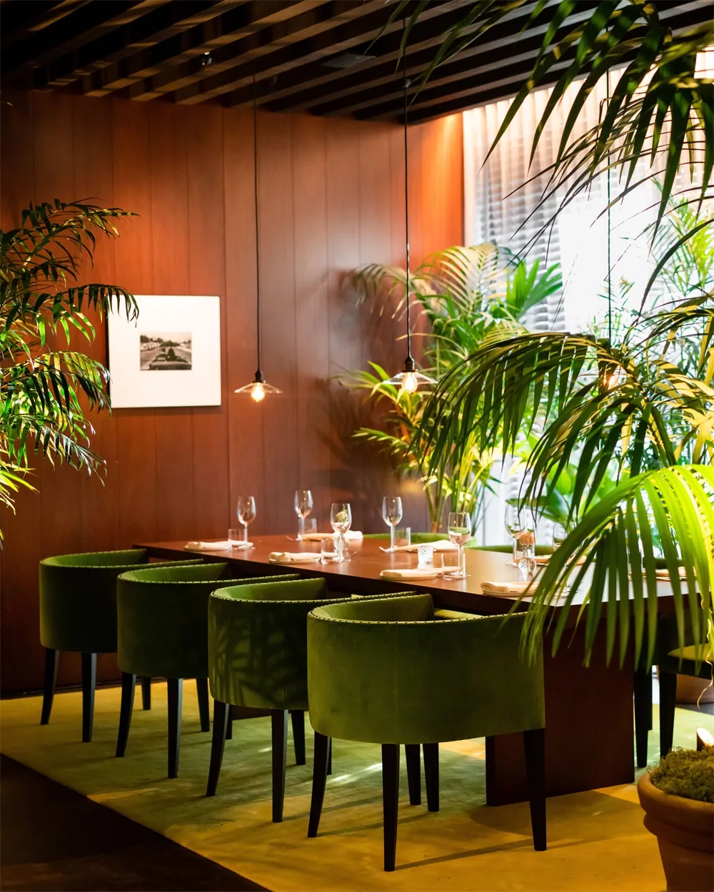 現代工業風餐廳內部,配有深色木質餐桌、綠色絲絨椅,以及茂盛的綠色植物。