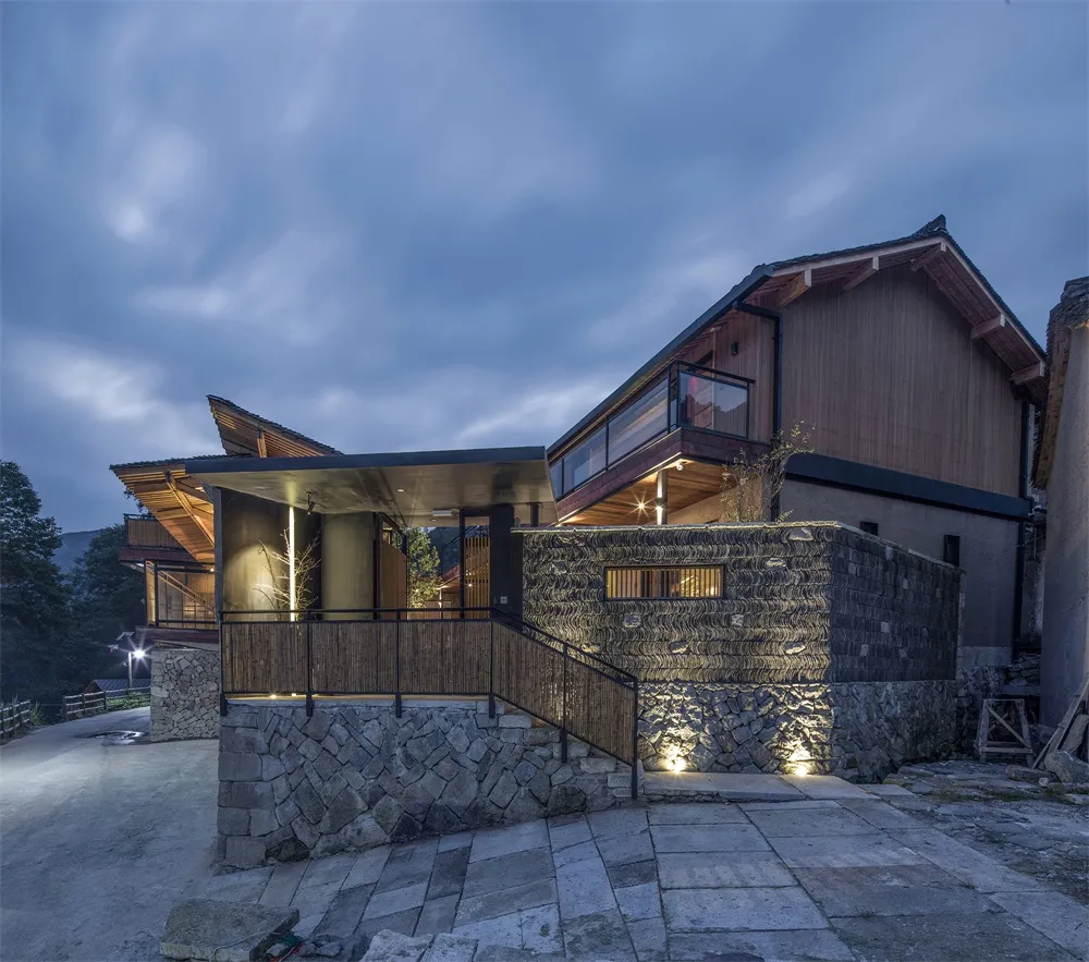 Modestly illuminated exterior of a modern residential building featuring mixed materials of wood and stone.