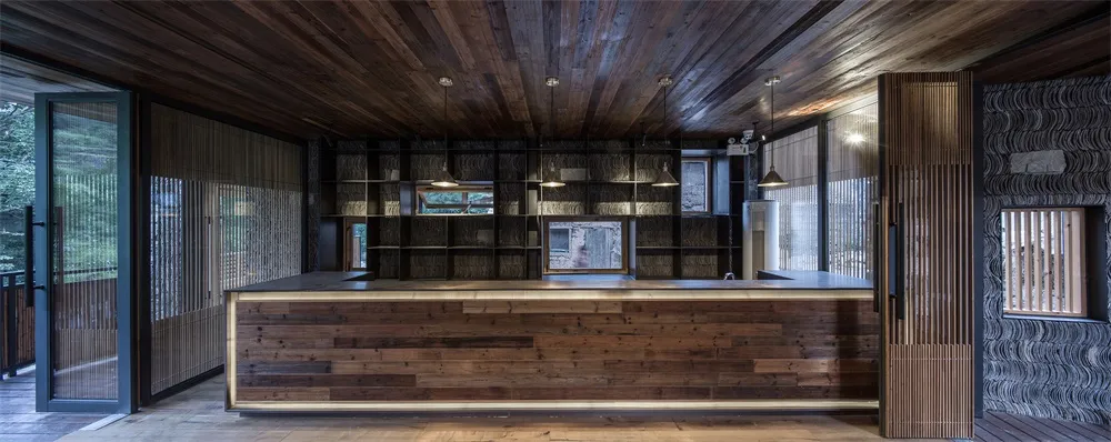 A warm wooden reception counter with integrated shelving and hanging lights.