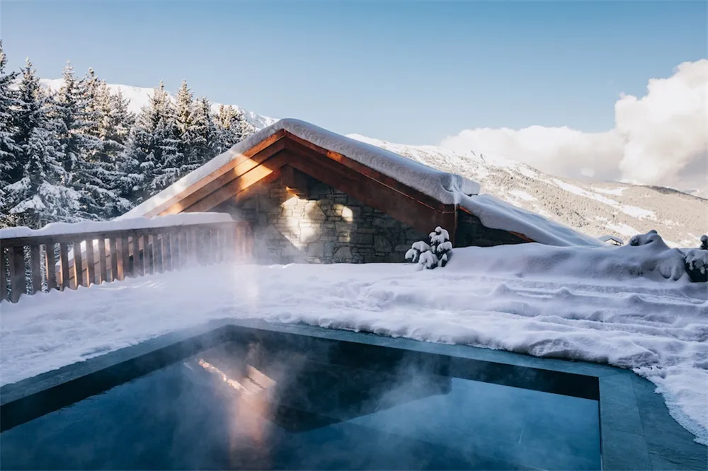 現代工業風泳池,水面升起霧氣,周圍被雪覆蓋的樹木與木質建築