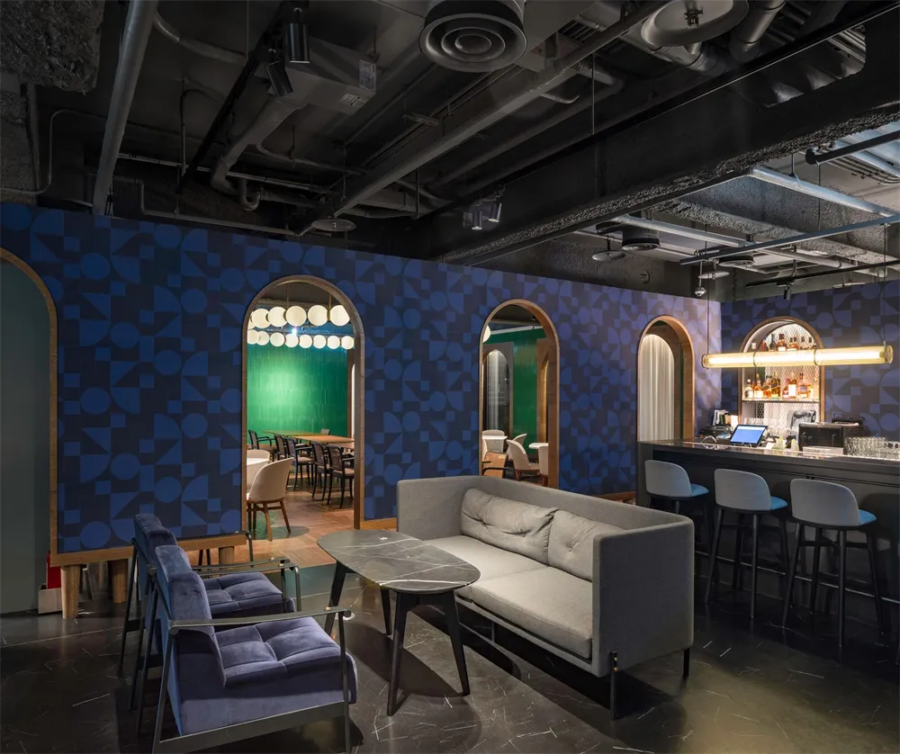 A modern cafe bar featuring a geometric patterned tile wall, painted accents, upholstered furniture, and a wooden floor.