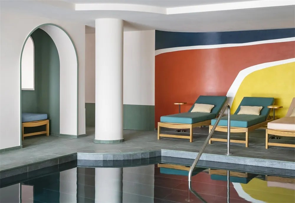 A modern spa interior featuring concrete flooring, colorful walls, and teal lounge chairs.