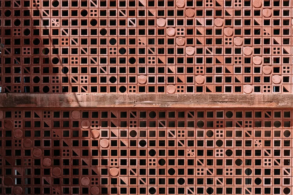 A wall featuring a design pattern made of red bricks with various geometric shapes and sizes.