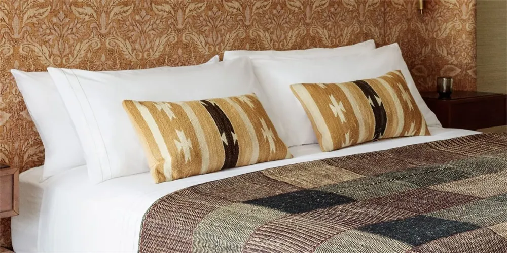 a bedroom with white bedding, tribal patterned pillows, and a patchwork quilt on a cozy bed