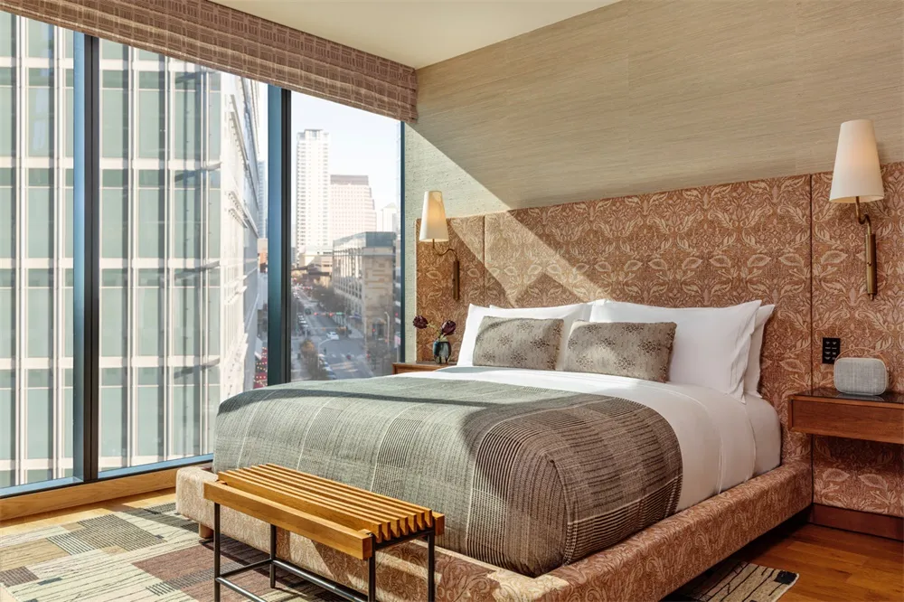 A modern bedroom featuring a patterned upholstered bed with a window view of a cityscape.