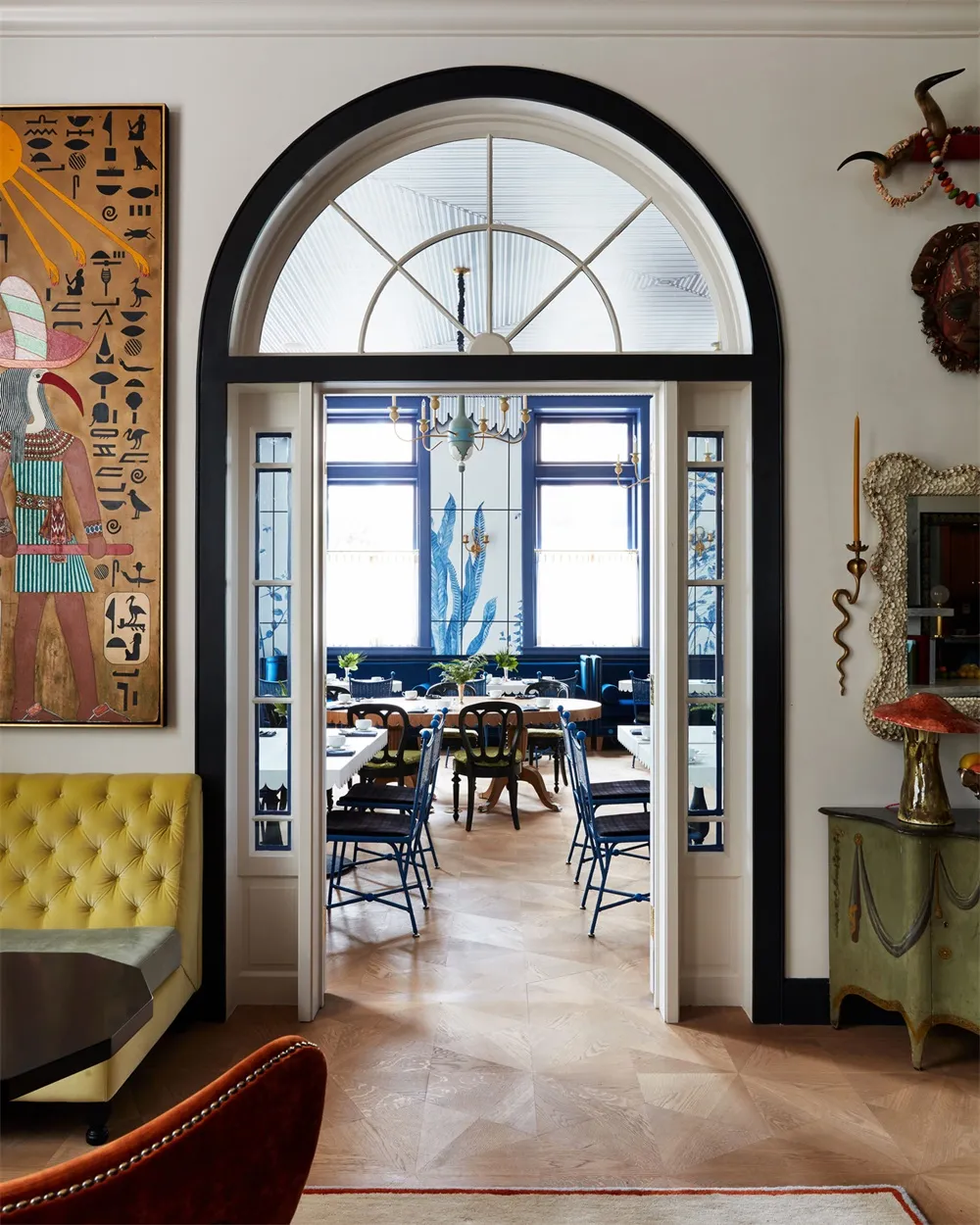 Modern dining room with wooden floors, chairs, and table, featuring a large arched window.