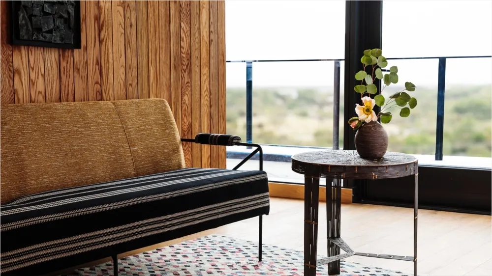 A modern interior with a wooden floor, featuring a sofa and a side table with a vase and flowers.