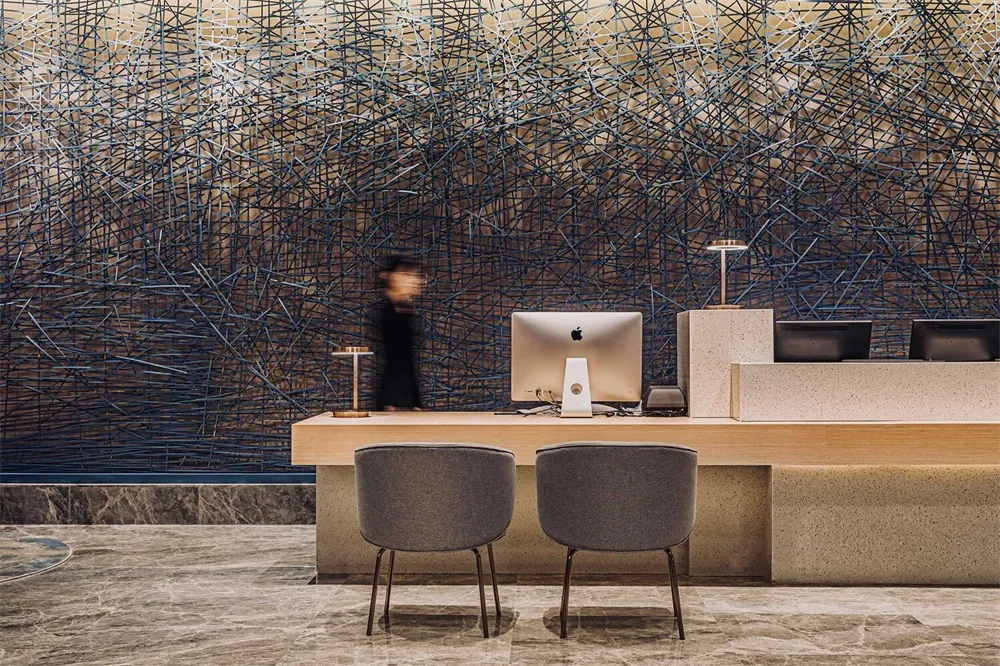 A modern reception desk featuring a metal cable net design with marble flooring and a blurred figure in the background.