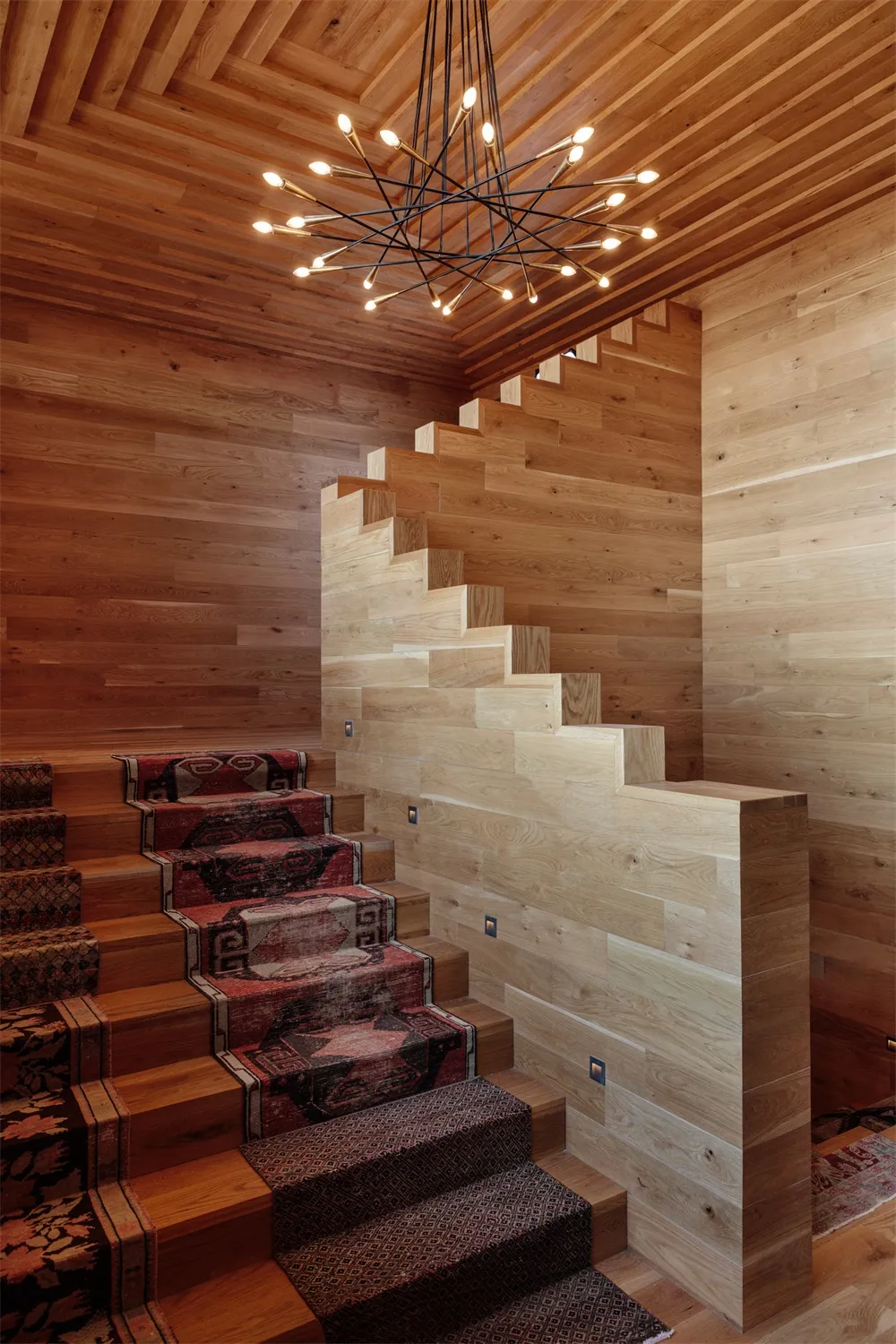 A modern staircase with wood paneling and a unique light fixture in a wooden room.