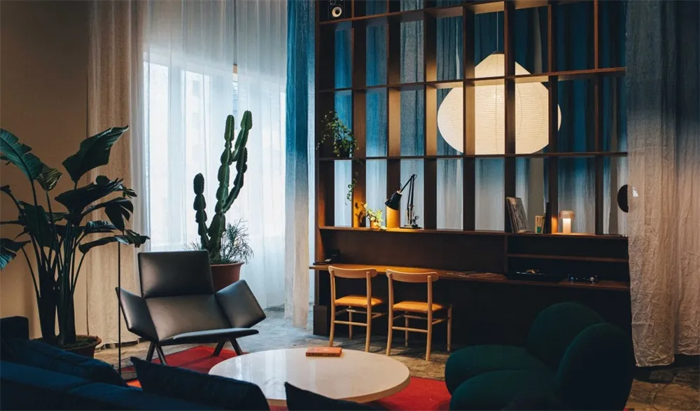Modern living room featuring glass windows, dark wood furniture, and greenery.