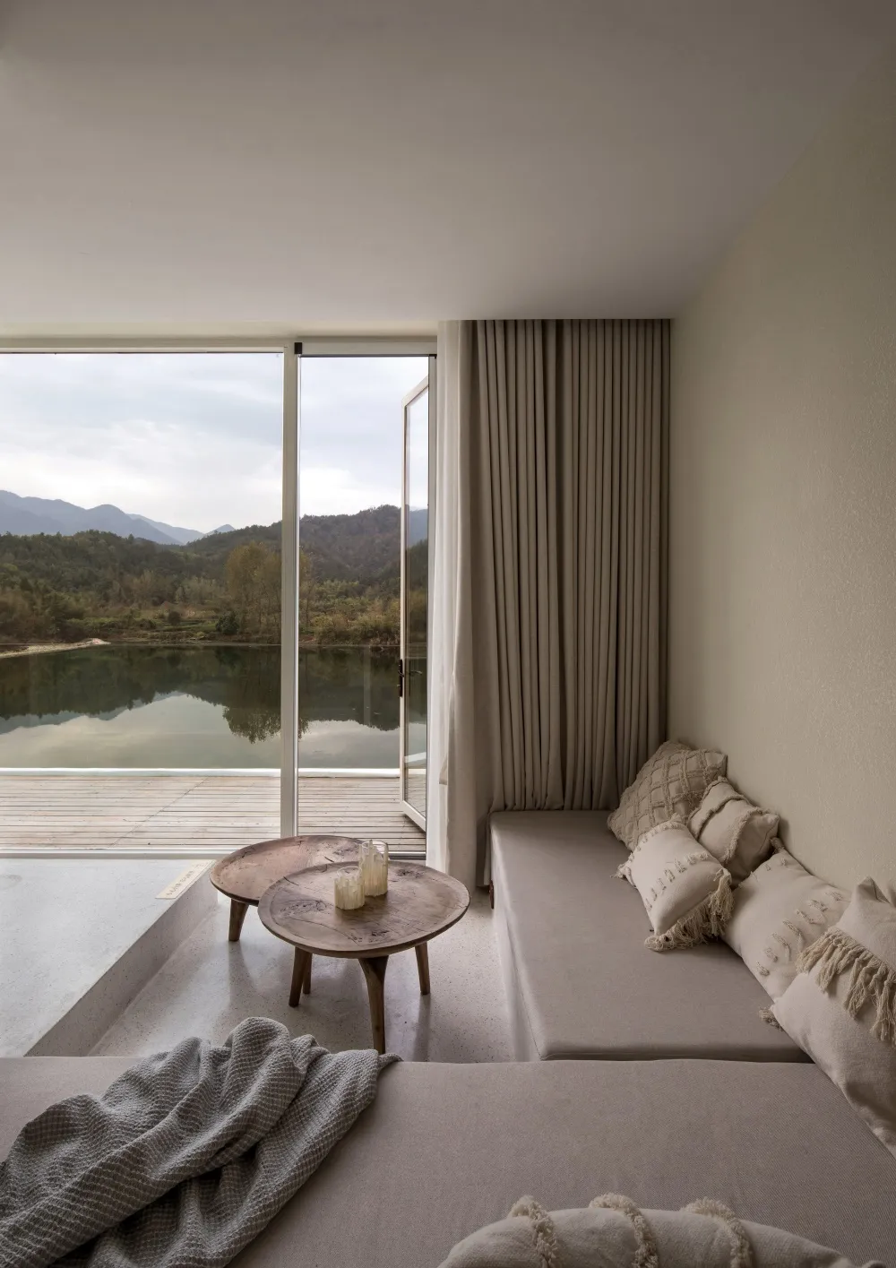 Modern minimalist living room with concrete walls and wooden furniture, featuring a cozy seating area with pillows, a small r