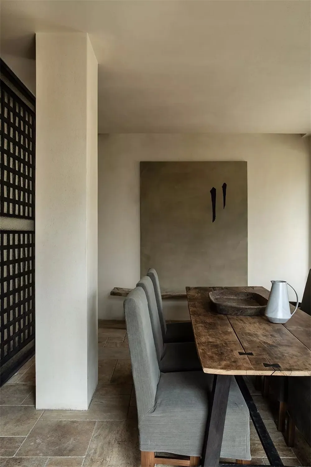Modern dining room with a wooden table, concrete walls, and upholstered chairs.