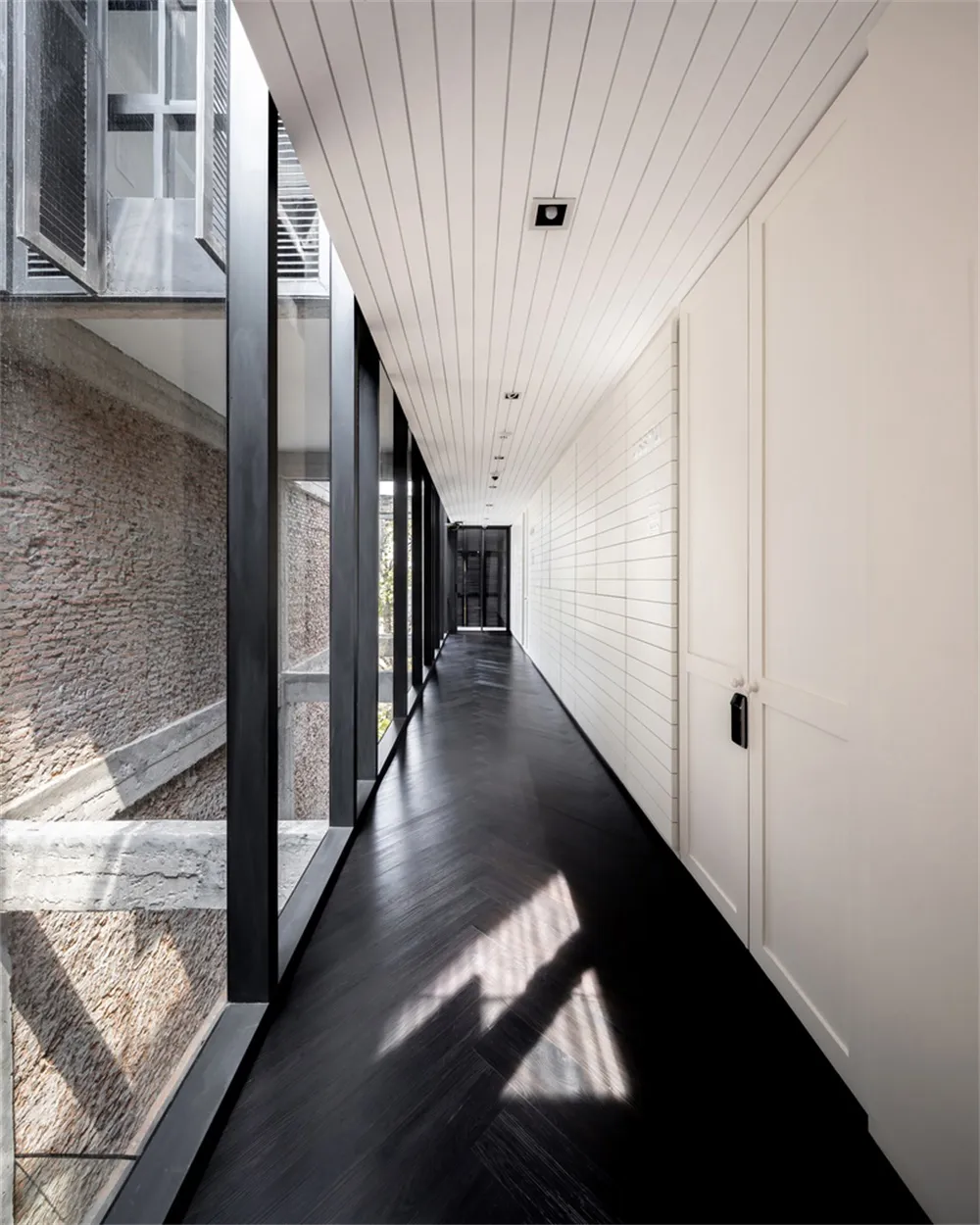 A modern white corridor with large glass windows and dark wooden flooring.