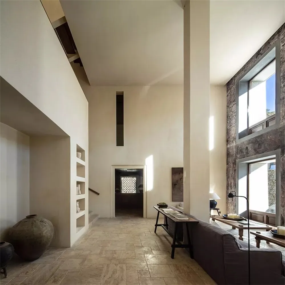 Modern minimalist living room with concrete flooring and walls, featuring a dark couch and a low table with books and decorat