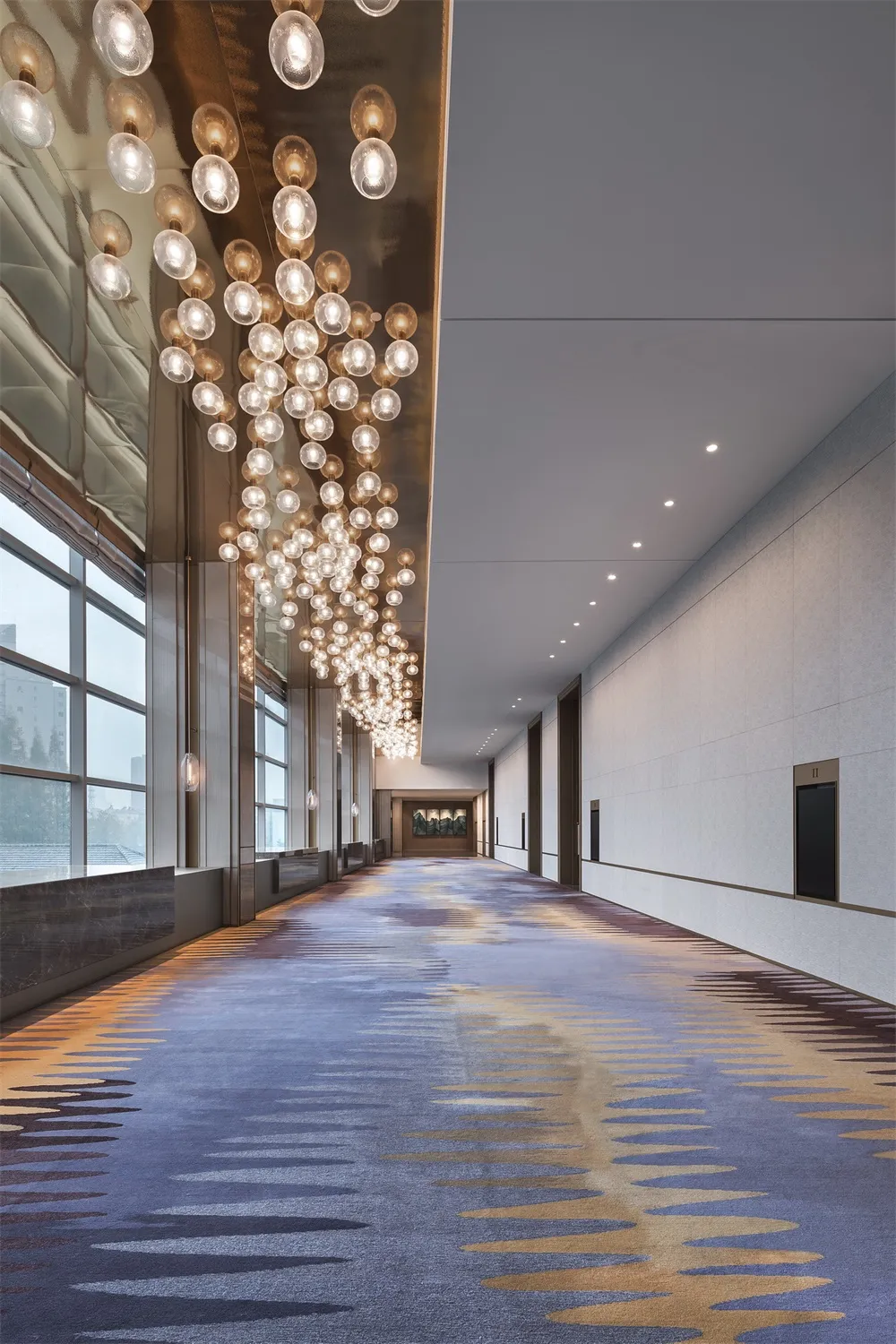 Long corridor with industrial design featuring marble walls and concrete floors, illuminated by modern lighting fixtures.