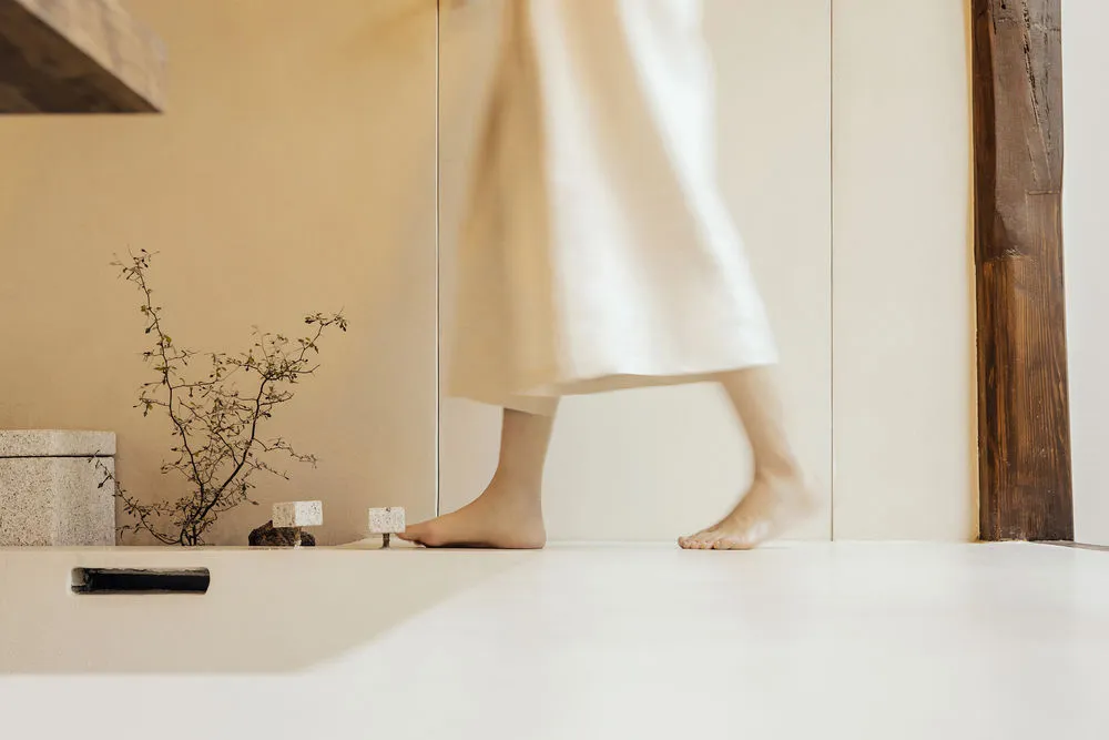 A minimalist room with white walls and a white floor, featuring a white plant and a wooden beam