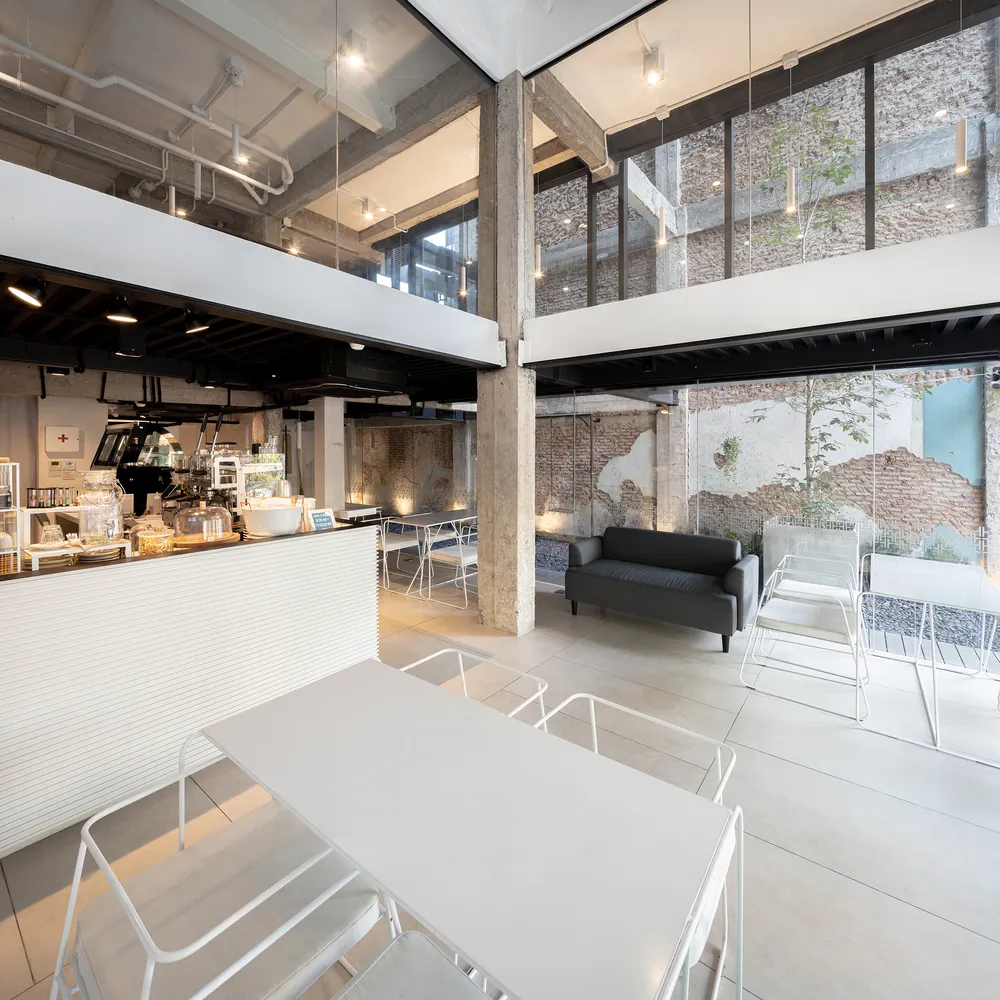 A modern industrial coffee shop with white concrete walls, white furniture, and a sleek design.