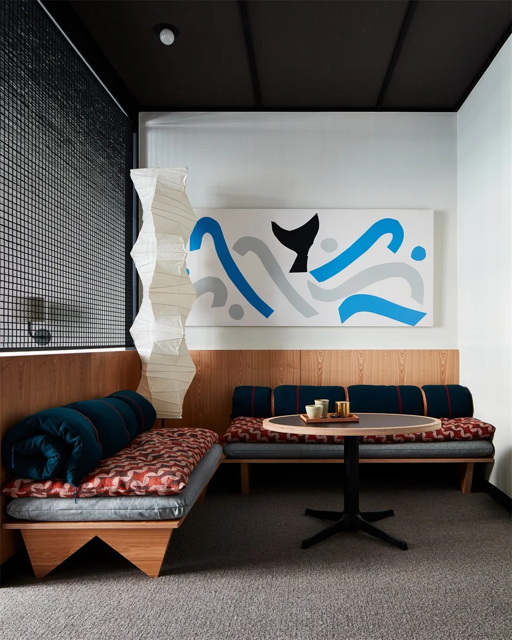 A modern cafe interior with wooden benches, fabric cushions, and a paper lantern.