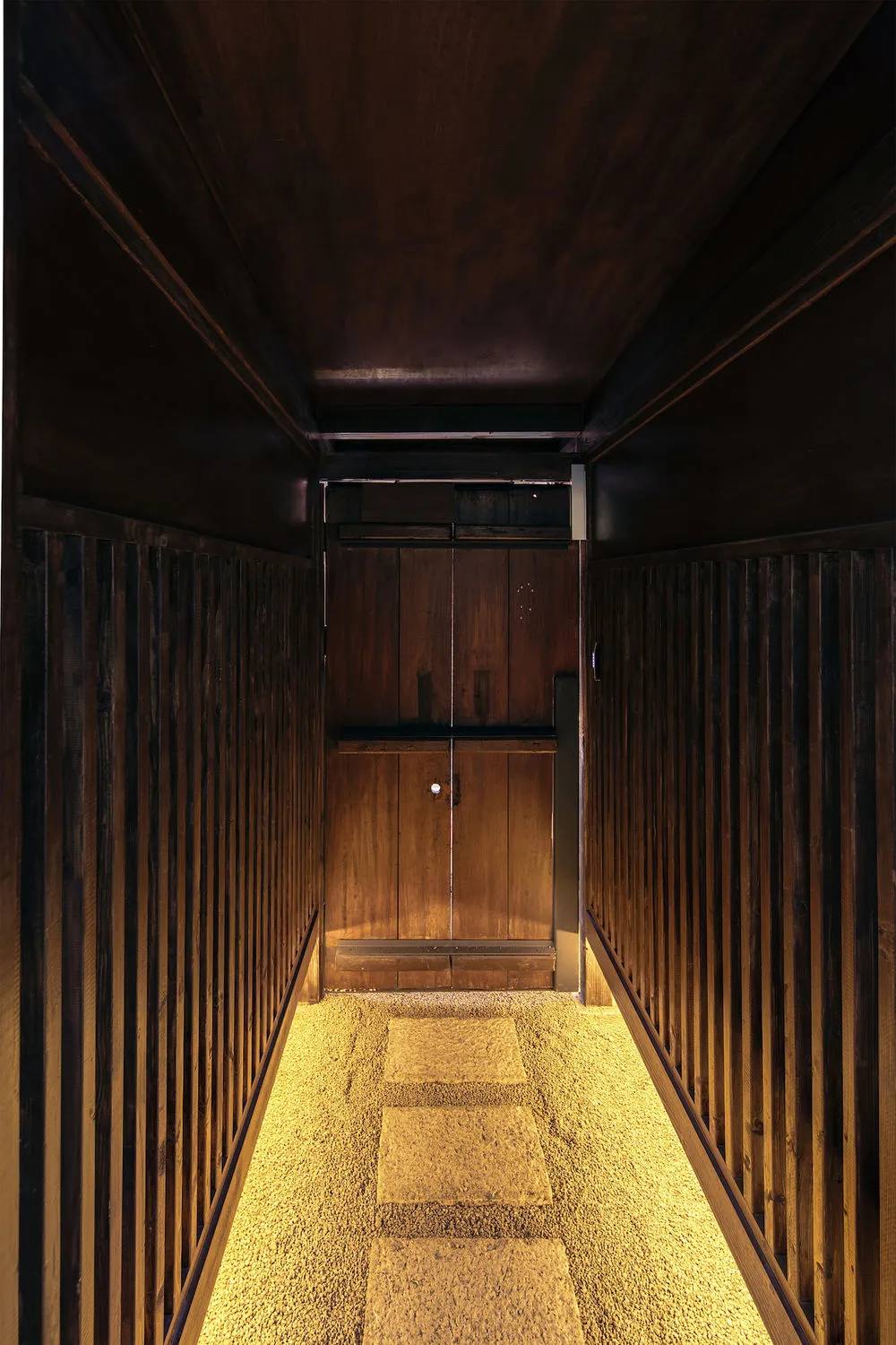 A narrow wooden corridor with textured carpet flooring and a wooden door at the end.