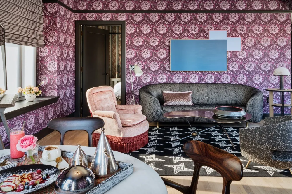 A modern living room with a patterned wallpaper, a grey sofa, and decorative elements like a pink flower arrangement and a gl
