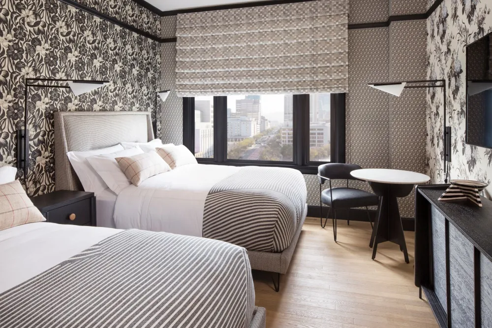 A modern hotel room featuring a bed with striped bedding and a window overlooking a cityscape, complemented by textured wallp