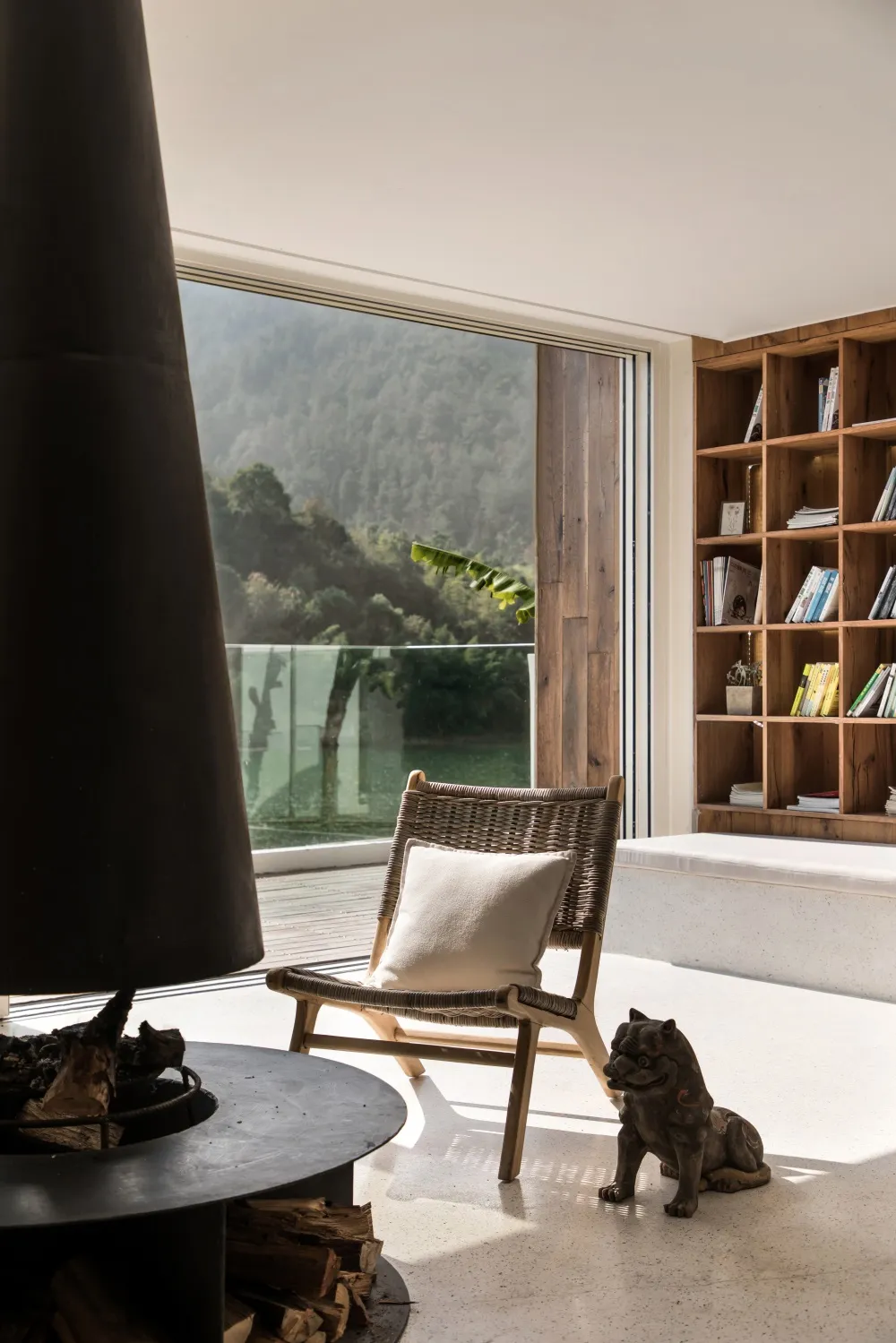 An inviting cozy living room with a wooden chair, concrete floor, and large window overlooking a scenic outdoor view.