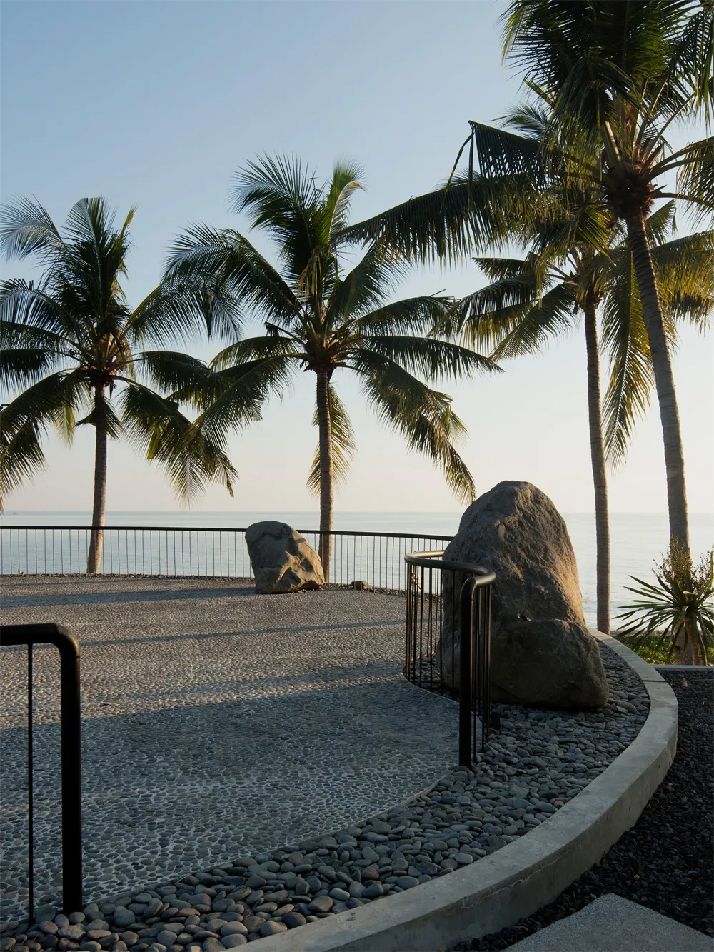Concrete path with large rocks and palm trees overlooking the ocean.