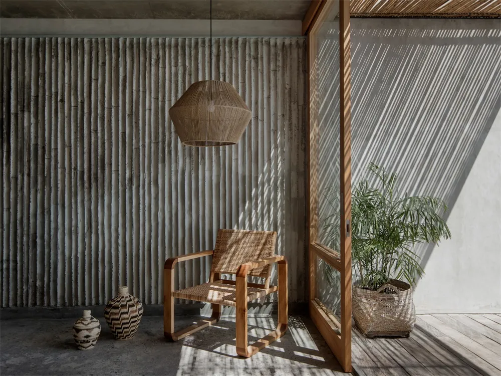A minimalist interior design featuring a concrete wall, wooden armchair, and rattan pendant light.