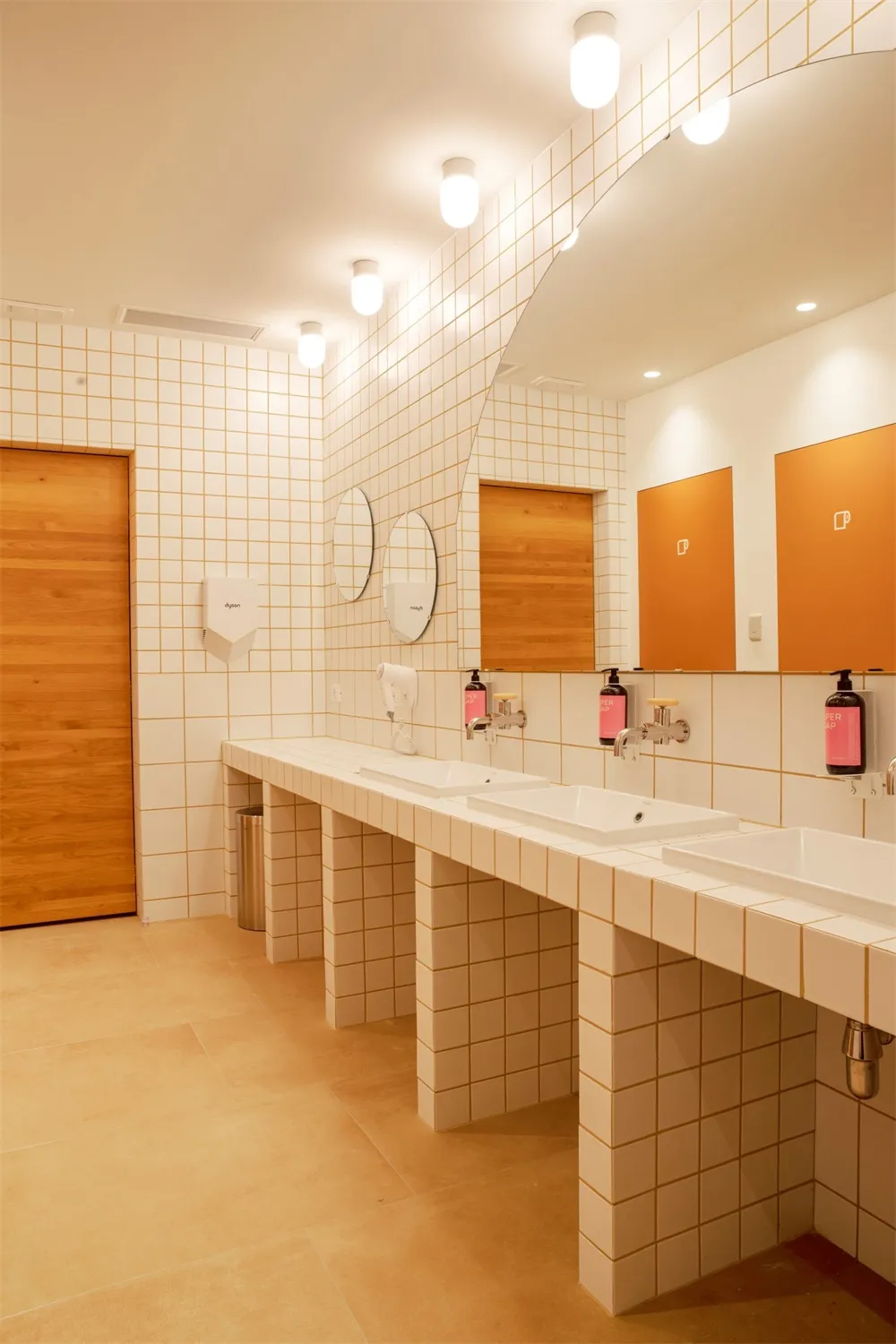 A modern industrial bathroom with white tiled walls and square tiles on the floor.