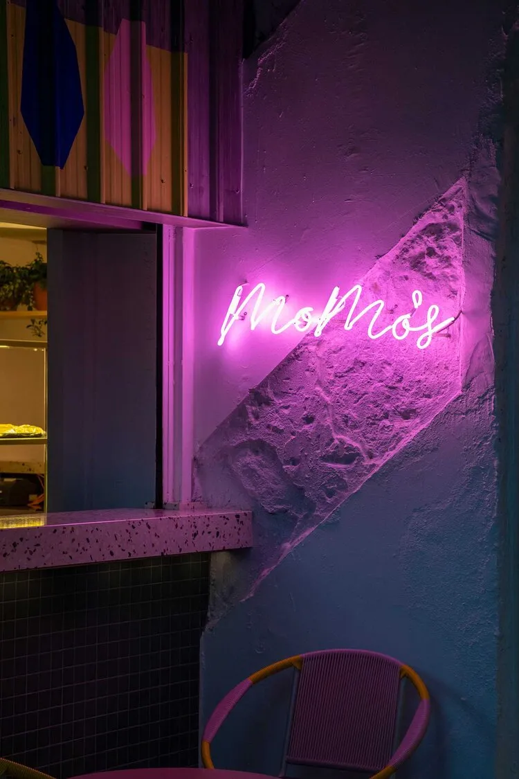 A modern bar area with pink neon lighting and a concrete wall.