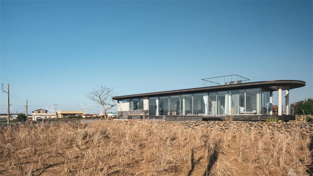 Modern house with glass exterior on a field of dry grass under a clear blue sky.