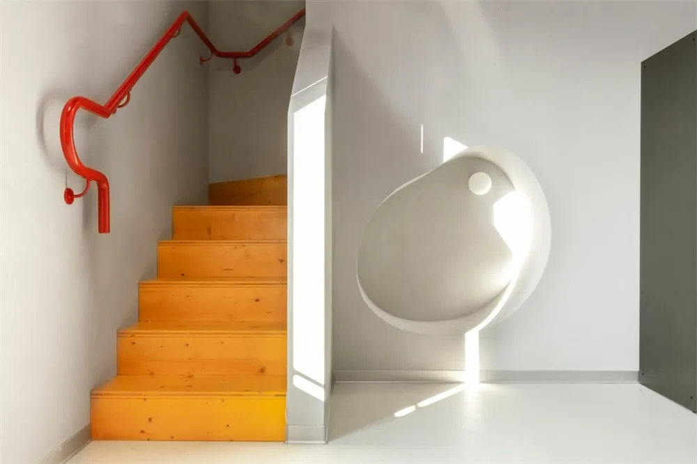 Modern staircase with orange steps and a red handrail.