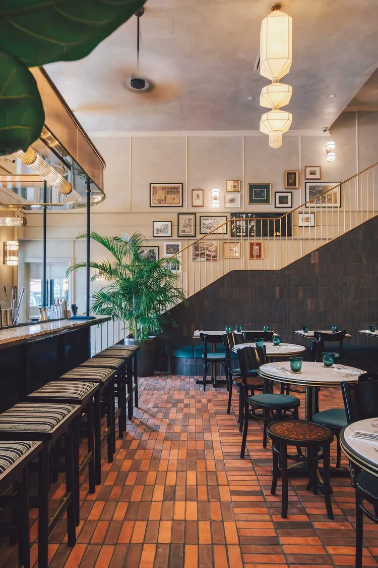The interior design of a brass bar restaurant showcases a stylish, modern space with brick tile flooring, green foliage, and 